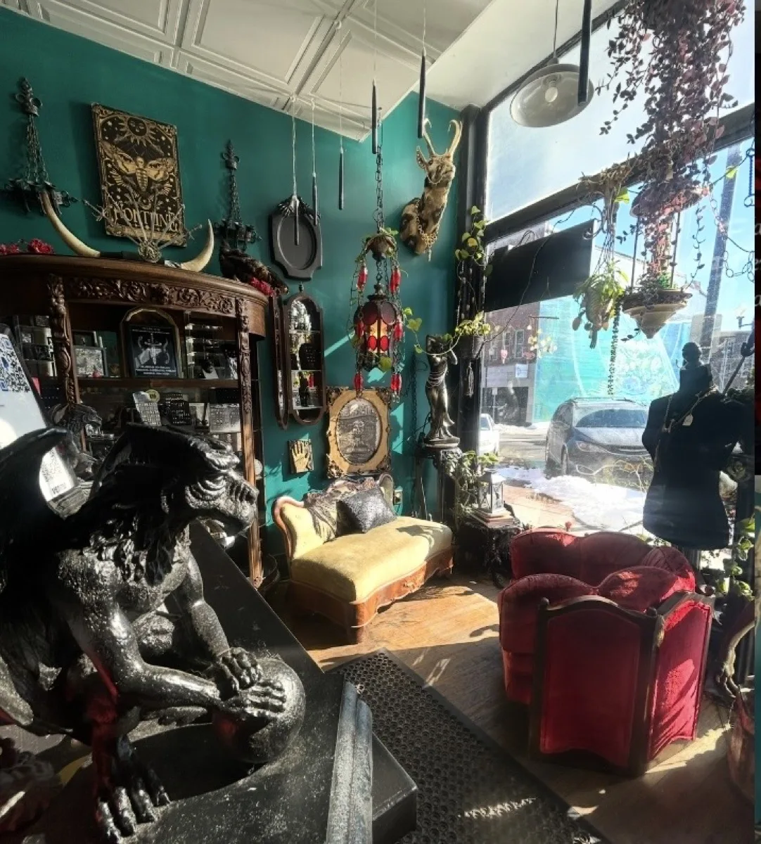 Ornate parlor interior with gargoyle sculpture, hanging plants, and stained glass lanterns